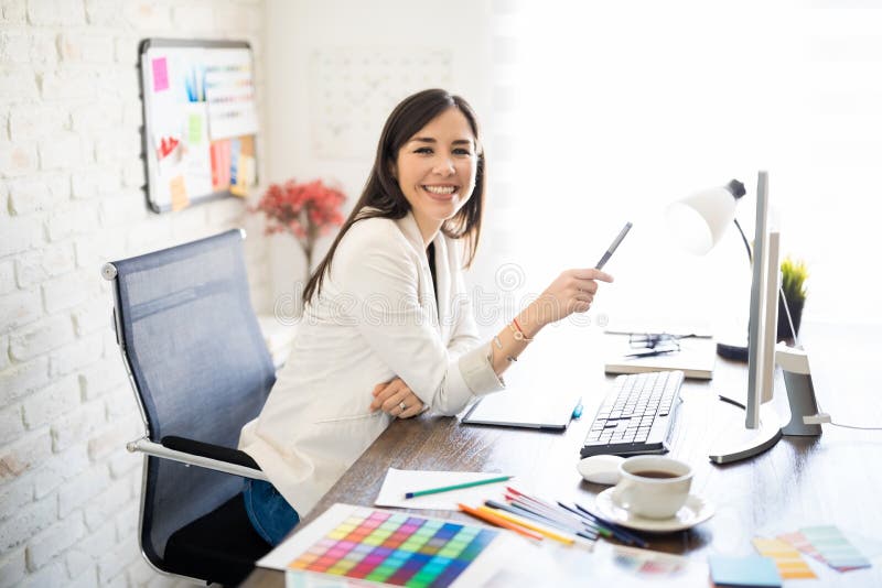 Portrait of a good looking woman graphic designer working at her desk and making an eye contact. Portrait of a good looking woman graphic designer working at her desk and making an eye contact