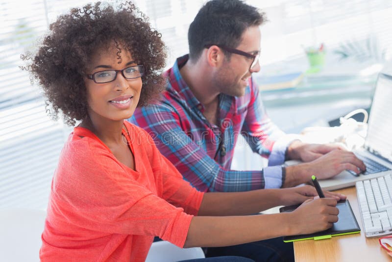 Graphic designer using a graphics tablet in her office with a colleague working behind. Graphic designer using a graphics tablet in her office with a colleague working behind