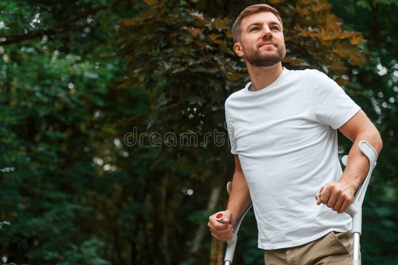 Disfrutando del paseo. hombre con muletas está en el parque al aire libre. lesión en la pierna imágenes de archivo libres de regalías