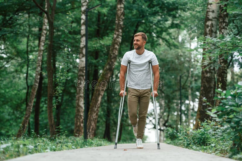 Disfrutar de la naturaleza. hombre con muletas está en el parque al aire libre. lesión en la pierna imagen de archivo