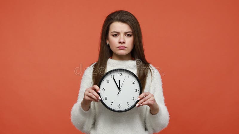 Disgustada mujer impaciente apuntando a la pantalla del reloj de pared pidiendo que se apure