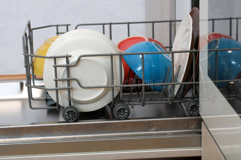 Dishwasher-korg lastad med färgplattor och skålar som gör sig redo för arkivfoto