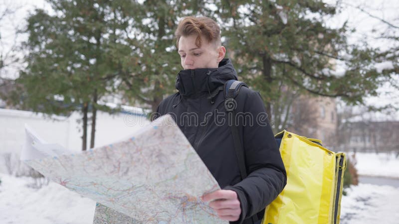 Disoriented young man with food delivery backpack using paper map searching for delivering address. Portrait of handsome stock video