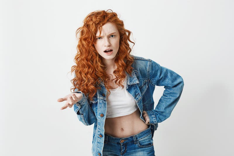 Displeased brutal redhead girl looking at camera not understanding over white background. Copy space.