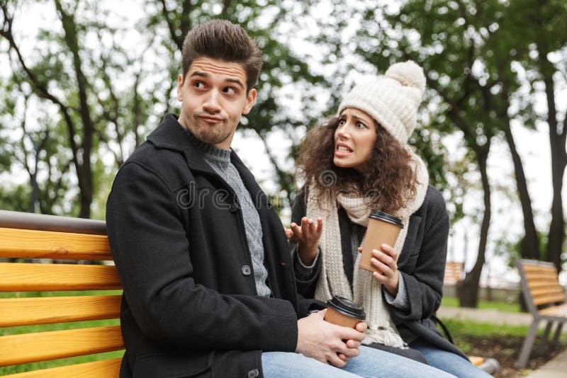 Displeased forçou o ar livre bebendo de amor novo do chá ou do café dos pares no parque que fala um com o otro a discussão fotografia de stock Displeased forçou o ar livre bebendo de amor novo do chá ou do café dos pares no parque que fala um com o otro a discussão fotografia de stock