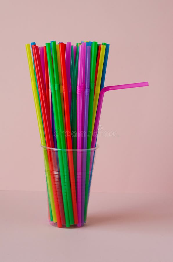 Disposable Plastic Colored Straws in a Plastic Cup on a Pink Background