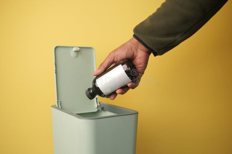 Disposing of a bottle in a green trash bin with a yellow background stock image
