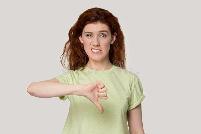 Dissatisfied young red-haired woman showing thumbs down gesture, unhappy female customer giving negative feedback on product or service, does not recommend store, isolated on studio background. Dissatisfied young red-haired woman showing thumbs down gesture, unhappy female customer giving negative feedback on product or service, does not recommend store, isolated on studio background.