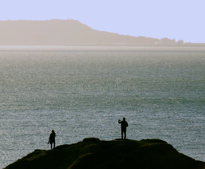 Silhouette of a couple on a cliff top with man taking a selfie stock photo Silhouette of a couple on a cliff top with man taking a selfie stock photo
