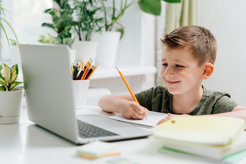 Distansutbildning online. Kaukasisk leende pojke som studerar hemma med en bärbar dator och gör skolläxor arkivbild