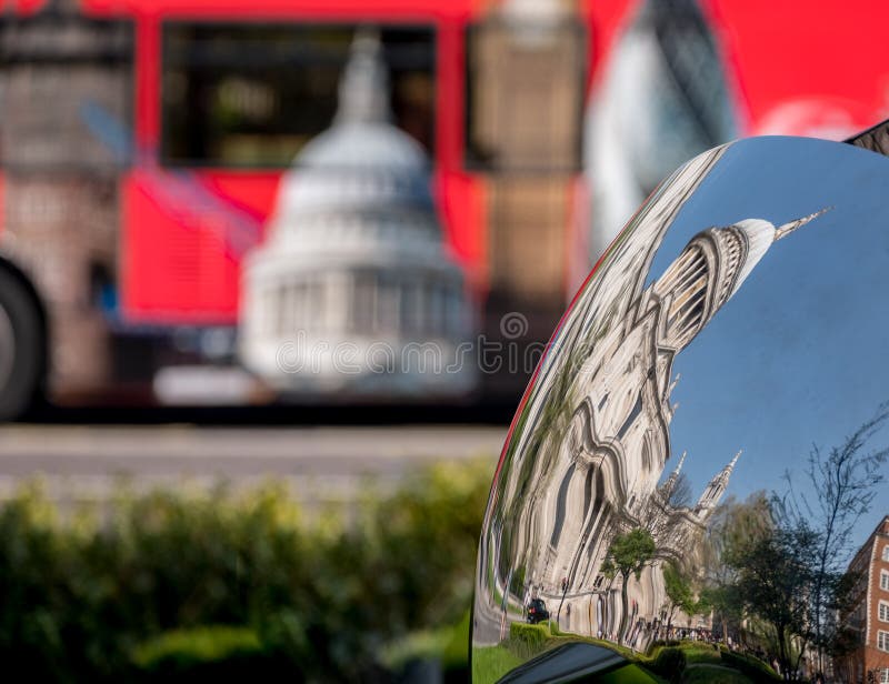 Distorted reflection of St Paul`s Cathedral, reflected in surface of mirror sculpture. Blurred red London bus in background. stock photos