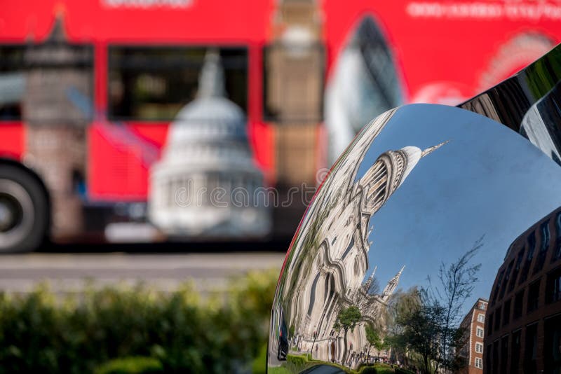 Distorted reflection of St Paul`s Cathedral, reflected in surface of mirror sculpture. Blurred red London bus in background. royalty free stock photography