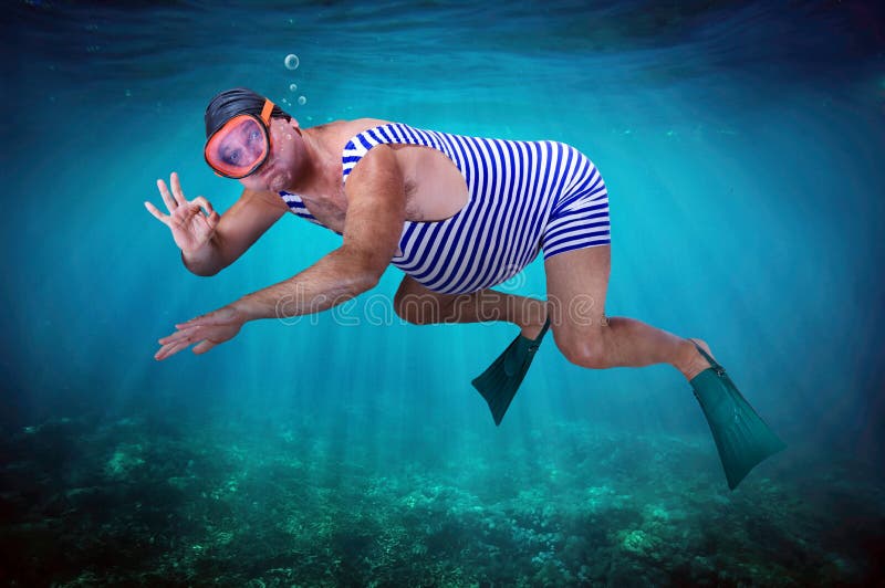 Diver in retro swimsuit swims underwater and shows gesture O.K. Swimmer examines the seabed. Vacation at sea. Man snorkeling in the tropical sea. Vintage style man with flippers diving under water.