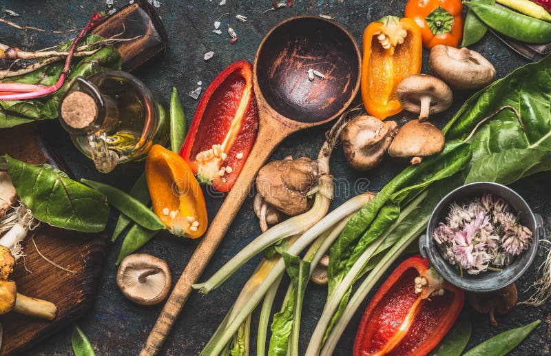 Divers légumes frais avec la cuillère à cuire en bois pour la consommation et la nutrition saines sur le fond rustique foncé