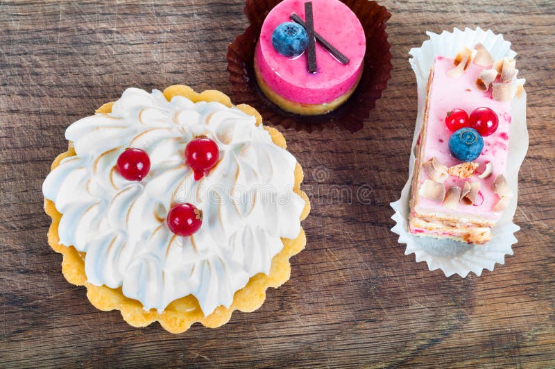 Different sort of beautiful pastry, small colorful sweet cakes on wooden board. Different sort of beautiful pastry, small colorful sweet cakes on wooden board