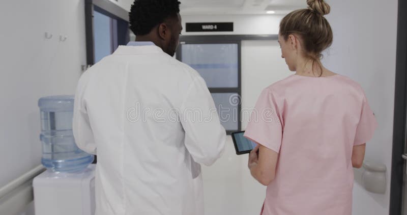 Diversas enfermeras y doctores varones caminan por el pasillo utilizando tablets y hablando a cámara lenta almacen de video