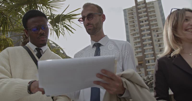 Diverse företagsgrupper samarbetar om ett projekt som granskar dokument och inleder diskussioner utomhus lager videofilmer
