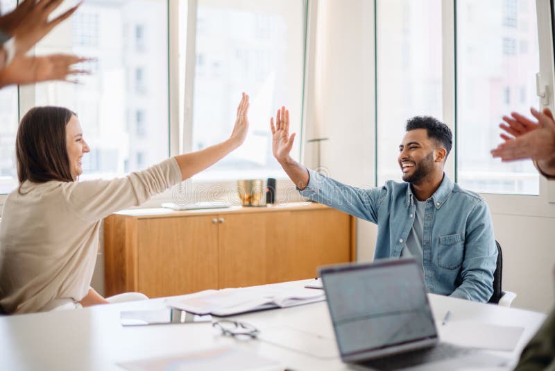 A diverse group of professionals in a modern office celebrates success with a high-five stock images