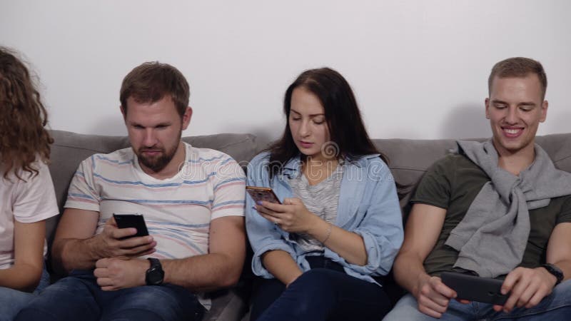 Diverse jongeren die in rij op laag zitten samen geobsedeerd met apparaten het online, Kaukasische verslaafden hun gebruiken