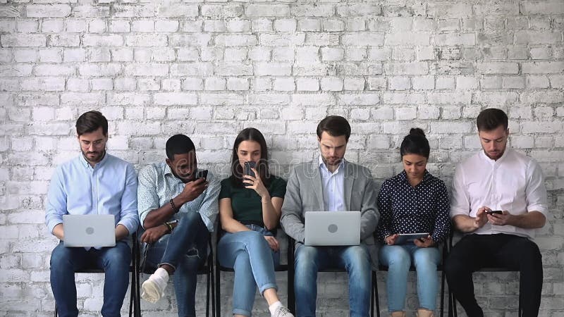 Diverse jongeren met gadgets die wachten op een sollicitatiegesprek.