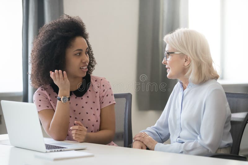 Diverse old and young female colleagues talking at work