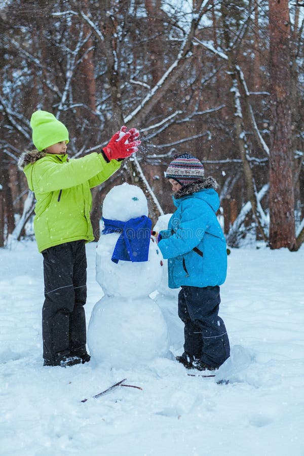 Diversión, niños felices que juegan con el muñeco de nieve en parque del invierno imagen de archivo Diversión, niños felices que juegan con el muñeco de nieve en parque del invierno imagen de archivo