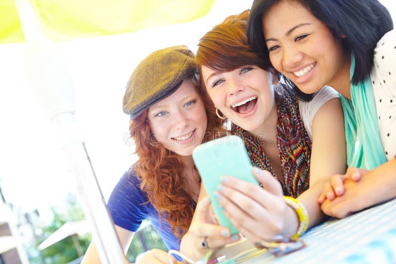 Technological fun. A group of adolescent girls laughing as they look at something on a smartphone screen. Technological fun. A group of adolescent girls laughing as they look at something on a smartphone screen