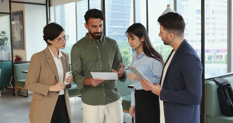 Diverso equipo de negocios de cuatro jóvenes colegas discutiendo un documento financiero metrajes