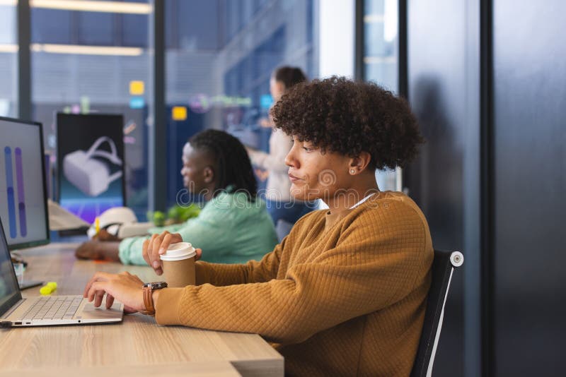 Diverse colleagues focusing on work in modern office using laptops. Biracial man with curly hair holding coffee, African American man viewing VR graphs, unaltered. Diverse colleagues focusing on work in modern office using laptops. Biracial man with curly hair holding coffee, African American man viewing VR graphs, unaltered