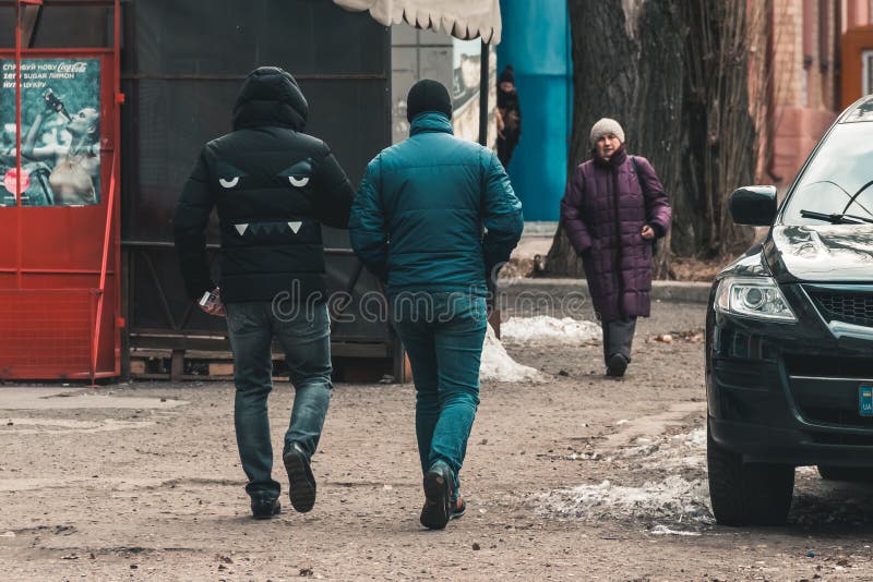 DNIPRO, UKRAINE - March 2, 2019: Two men walking down the street. Bulldog face design on coat back. Coca-Cola advertising poster