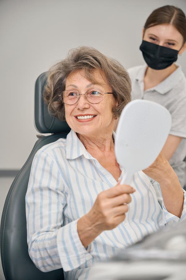 Doamna cu părul alb în birou stomatologic cu oglinda în mâini stock photos