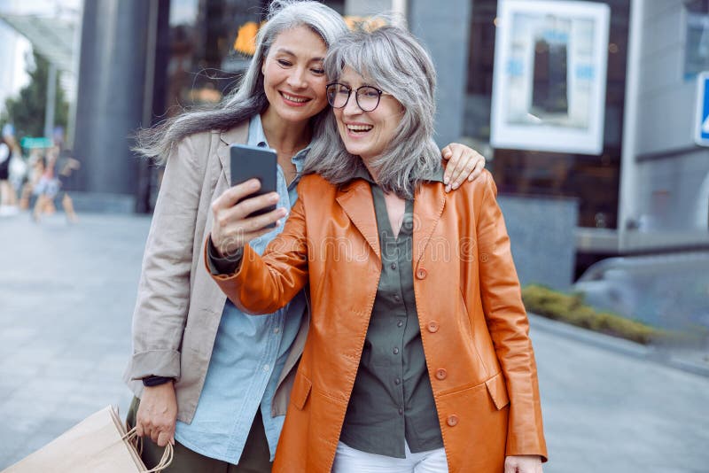 Doamna cu părul frumos și însoțitoare cu saci de cumpărături iau selfie pe strada modernă a orașului royalty free stock image