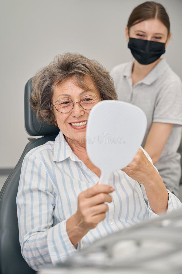 Doamna cu părul gri își examinează dinții în oglindă royalty free stock photo