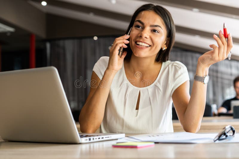 Dobra biznesowa rozmowa Rozochocona młoda piękna kobieta opowiada na telefonie komórkowym i używa laptop z uśmiechem przy podczas
