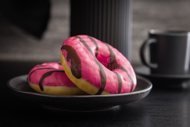 Doce donut cor-de-rosa com faixas de chocolate num prato sobre uma mesa preta imagem de stock
