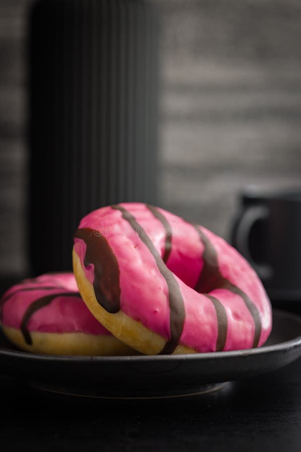 Doce donut cor-de-rosa com listras de chocolate num prato sobre uma mesa preta foto de stock royalty free