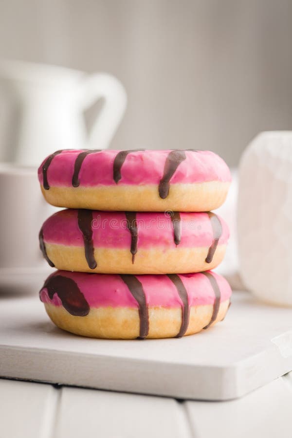 Doce donut cor-de-rosa com listras de chocolate sobre uma mesa branca imagens de stock