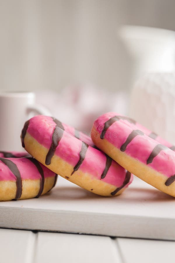 Doce donut cor-de-rosa com listras de chocolate sobre uma mesa branca imagem de stock