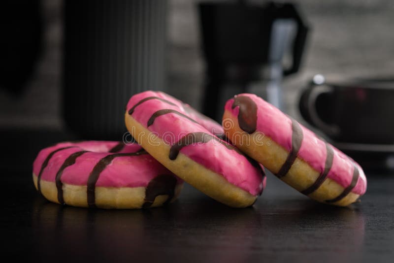 Doce donut cor-de-rosa com listras de chocolate sobre uma mesa preta fotografia de stock royalty free
