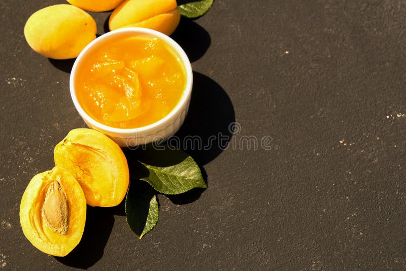 Doce orgânico caseiro do abricó na bacia branca e em abricós maduros no fundo preto Luz dura imagem de stock royalty free Doce orgânico caseiro do abricó na bacia branca e em abricós maduros no fundo preto Luz dura imagem de stock royalty free