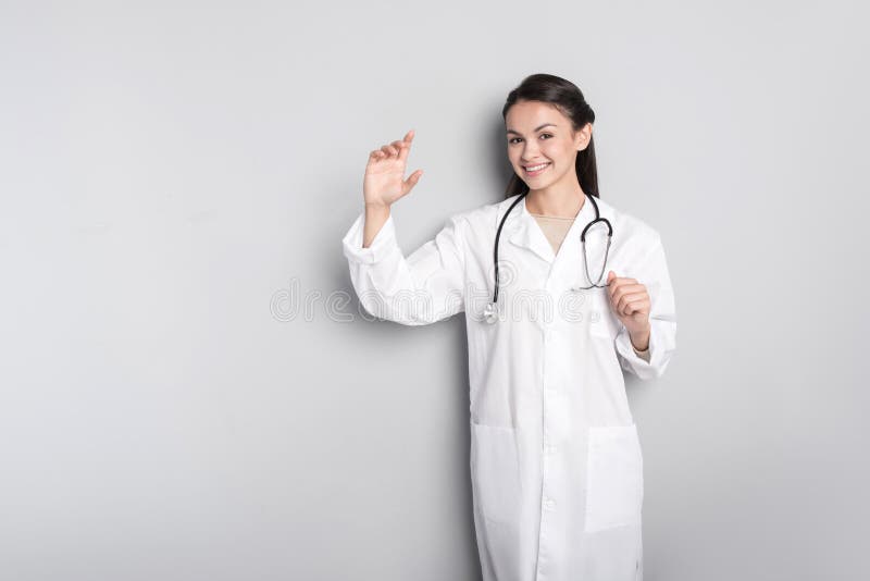 Docteur féminin professionnel joyeux se tenant sur le fond gris image stock Docteur féminin professionnel joyeux se tenant sur le fond gris image stock
