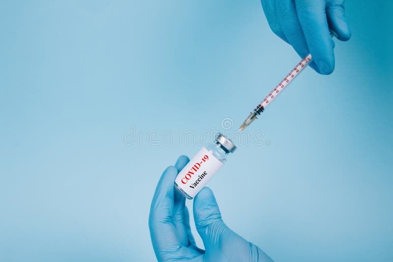 Doctor injecting vial dose of COVID-19 vaccine with syringe against blue background with copy space - prevention coronavirus, global vaccination concept, selective focus. Doctor injecting vial dose of COVID-19 vaccine with syringe against blue background with copy space - prevention coronavirus, global vaccination concept, selective focus