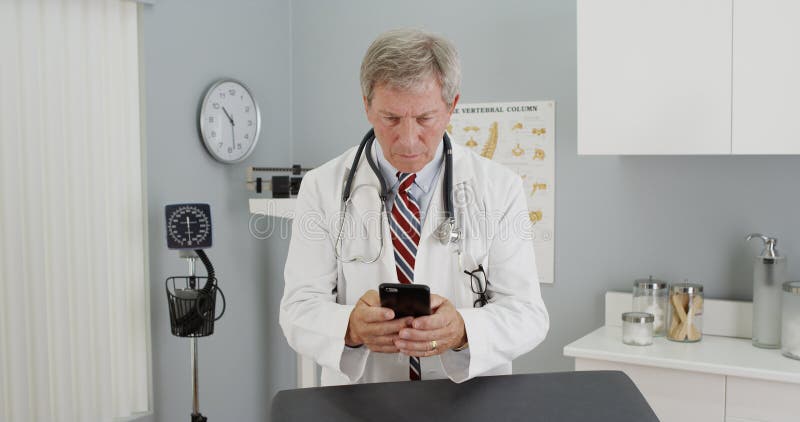 Docteur mûr à l'aide du smartphone dans le bureau image libre de droits Docteur mûr à l'aide du smartphone dans le bureau image libre de droits