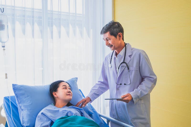Docteur masculin asiatique supérieur rendant visite au patient féminin d'une cinquantaine d'années sur la salle dans l'hôpital de image libre de droits Docteur masculin asiatique supérieur rendant visite au patient féminin d'une cinquantaine d'années sur la salle dans l'hôpital de image libre de droits