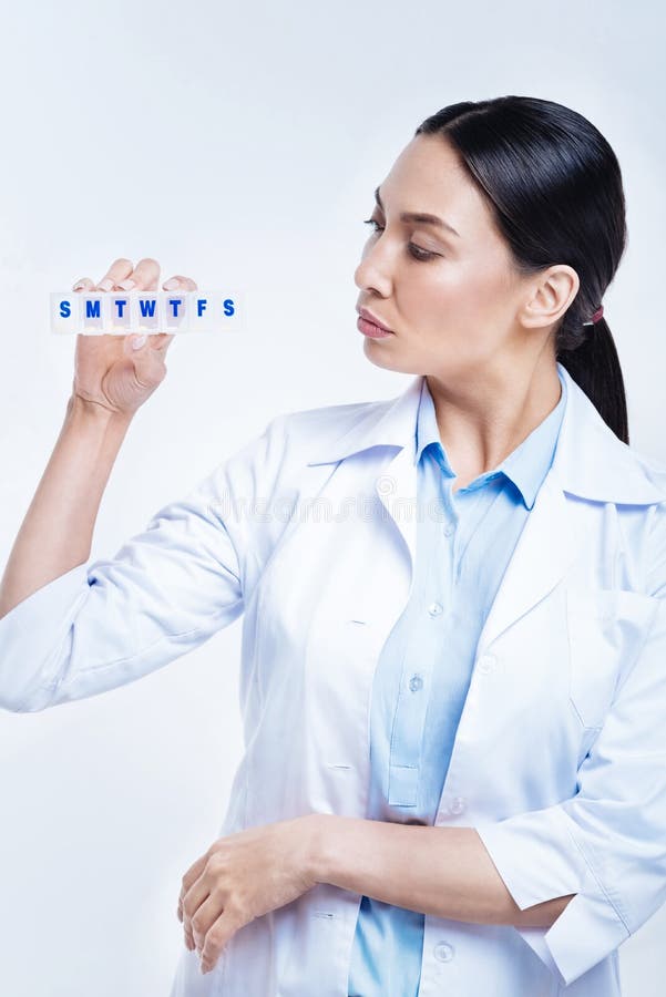 Doctor bastante de sexo femenino que mira al organizador de las píldoras en sus manos foto de archivo Doctor bastante de sexo femenino que mira al organizador de las píldoras en sus manos foto de archivo