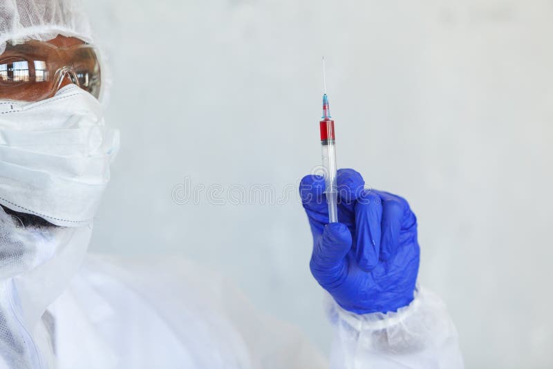 Doctor in chemical protection suit is holding syringe with blood sample fot testing it on COVID, COVID-19, coronavirus. To stop pandemic and epidemic of the royalty free stock photo Doctor in chemical protection suit is holding syringe with blood sample fot testing it on COVID, COVID-19, coronavirus. To stop pandemic and epidemic of the royalty free stock photo