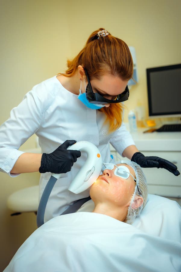 Doctor conducts procedure for rejuvenating facial skin with laser. Woman receiving facial beauty treatment, removing pigmentation royalty free stock photos
