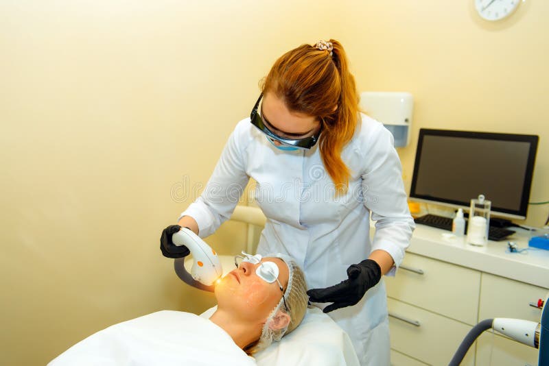 Doctor conducts procedure for rejuvenating facial skin with laser. Woman receiving facial beauty treatment, removing pigmentation stock photo