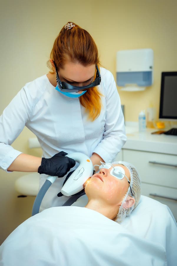 Doctor conducts procedure for rejuvenating facial skin with laser. Woman receiving facial beauty treatment, removing pigmentation stock image