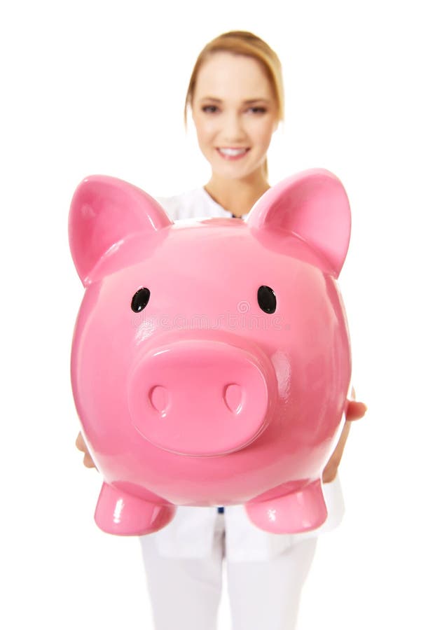 Doctor de sexo femenino joven que lleva a cabo un piggybank imágenes de archivo libres de regalías Doctor de sexo femenino joven que lleva a cabo un piggybank imágenes de archivo libres de regalías